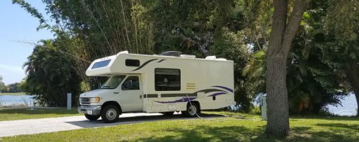 Gaye Lyn's 24'RV named Gracie, surrounded by lush trees and grass at lake's edge in John Price Park Campground, Lake Worth, FL.