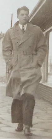 Young Dick Brougton in an overcoat with collar pulled up walking with a pilot's confidence. 